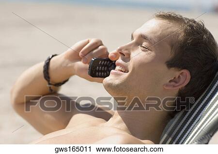 Stock Image - Side profile of a young man talking on a mobile phone. Fotosearch