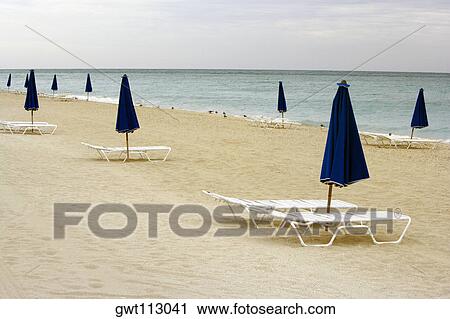 Empty lounge chair and a folded beach umbrella on the beach View Large Photo Image Stock Image - Empty lounge chair and a folded beach umbrella on the beach. Fotosearch