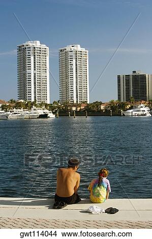 Rear view of a man and his daughter sitting on the edge of a pier View Large Photo Image Picture - Rear view of a man and his daughter sitting on the edge of a pier. Fotosearch