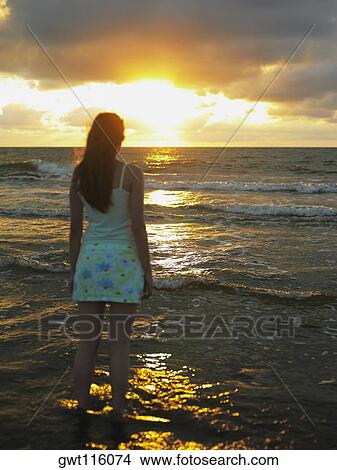 Picture - Rear view of a teenage girl standing on the beach. Fotosearch
