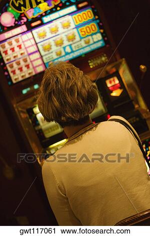 Stock Image - Rear view of a woman sitting in front of slot machine, Las Vegas, Nevada, USA. Fotosearch