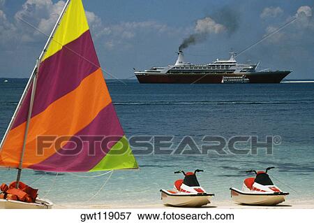 Stock Photo - Side view of a boat with a colorful sail with the Starship Majestic Cruise Ship in the background, Treasure Island, Bahamas. Fotosearch