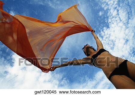 Stock Photography - Woman holding a orange colored fabric in the tropical breeze on the island of Barbados, Caribbean. Fotosearch