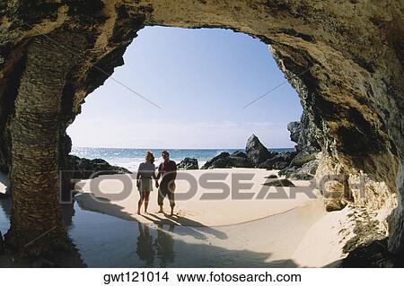 Picture - A couple observing rocks near the ocean, Natural arch, Bermuda. Fotosearch