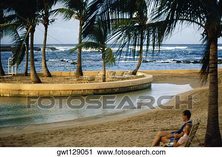 Stock Image - A couple is seen relaxing on a beach, Caribe Hilton, Puerto Rico. Fotosearch
