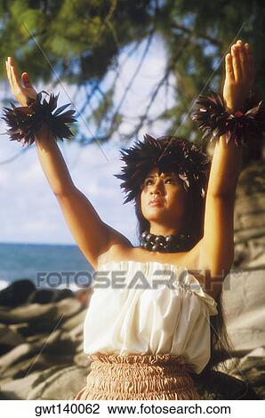 Stock Image - Close-up of a hula dancer standing on the beach with her arms raised, Hawaii, USA. Fotosearch