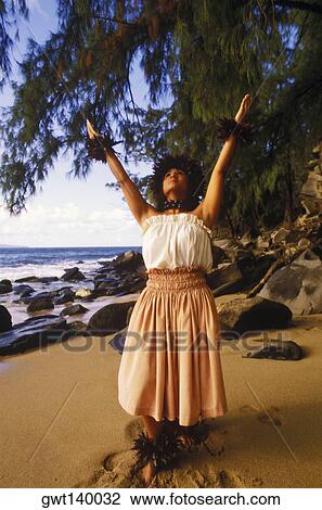 Stock Image - Hula dancer standing with her arms raised on the beach, Hawaii, USA. Fotosearch