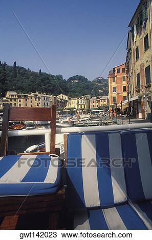 Stock Image - Close-up of ottoman against a railing overlooking boats in a harbor, Italy. Fotosearch