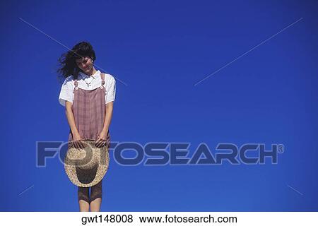 Low angle view of a young woman holding a sun hat View Large Photo Image Stock Photo - Low angle view of a young woman holding a sun hat. Fotosearch
