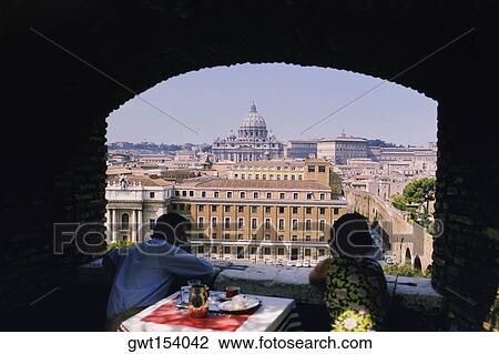 Stock Image - Tourists at a dining table looking at a basilica, St. Peter's Basilica, Rome, Italy. Fotosearch