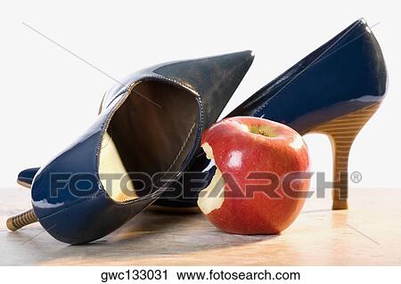 Stock Image - Close-up of a pair of high heels and an apple with a missing bite. Fotosearch