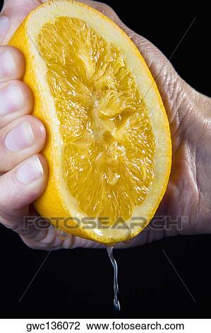 Stock Image - Close-up of a person's hand squeezing a tangerine. Fotosearch