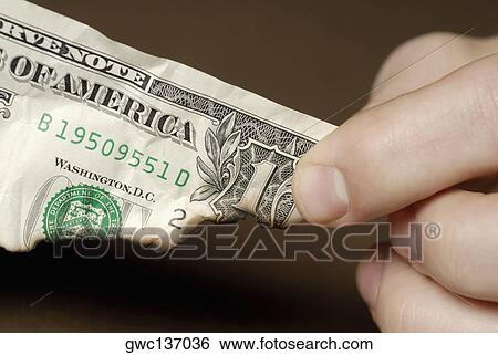 Stock Photograph - Close-up of a person's fingers holding a burnt American dollar bill. Fotosearch