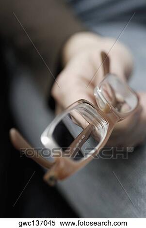 Stock Photography - Close-up of a person's hand holding a pair of eyeglasses. Fotosearch