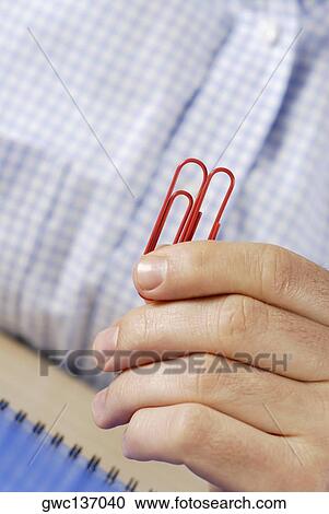 Stock Image - Close-up of a person's hand holding two paper clips. Fotosearch