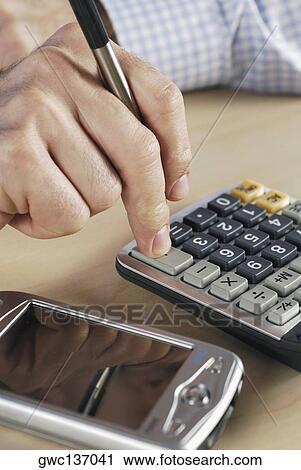 Stock Image - Close-up of a person's hand using a calculator. Fotosearch