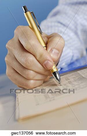 Stock Photograph - Close-up of a person's hand writing with a ballpoint pen on a sheet of paper. Fotosearch