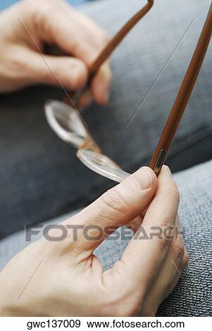 Close-up of a person's hands holding a pair of eyeglasses View Large Photo Image Stock Photo - Close-up of a person's hands holding a pair of eyeglasses. Fotosearch