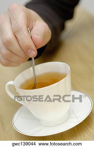 Picture - Close-up of a person's hand stirring tea with a teaspoon. Fotosearch