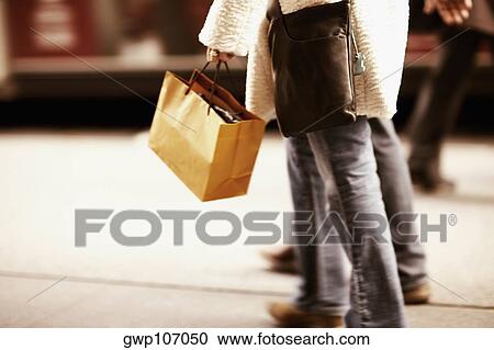Stock Image - Low section view of a person carrying a shopping bag. Fotosearch