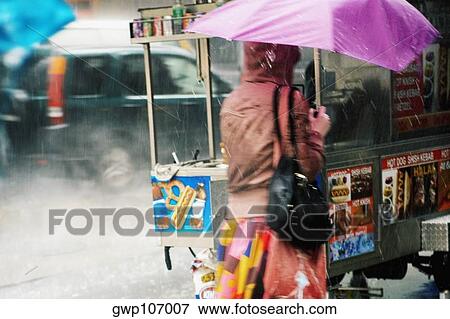 Stock Photo - Rear view of a woman holding an umbrella and walking. Fotosearch