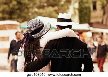 Stock Image - Rear view of a man and a woman with their arms around each other. Fotosearch