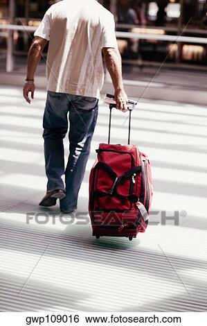 Stock Photograph - Rear view of a man walking and pulling luggage, Madrid, Spain. Fotosearch