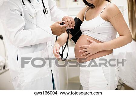 Picture - Male doctor checking a pregnant woman's blood pressure. Fotosearch