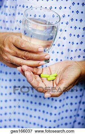 Stock Photo - Mid section view of a woman holding a glass of water and pills. Fotosearch