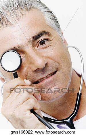 Portrait of a male doctor holding a stethoscope in front of his eyes View Large Photo Image Stock Image - Portrait of a male doctor holding a stethoscope in front of his eyes. Fotosearch