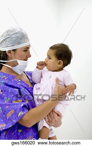 Stock Image - Side profile of a female doctor holding a baby girl sucking her thumb. Fotosearch