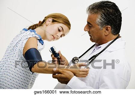 Stock Image - Side profile of a male doctor measuring blood pressure of a young woman. Fotosearch