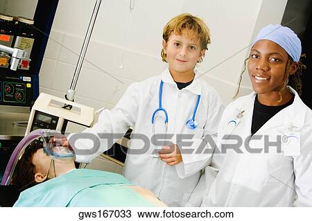 Stock Image - Boy imitating a doctor and adjusting the oxygen mask of a patient with a female doctor standing beside him. Fotosearch