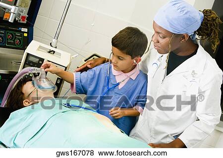 Boy imitating a doctor and adjusting the oxygen mask of a patient with a female doctor standing beside him View Large Photo Image Stock Photo - Boy imitating a doctor and adjusting the oxygen mask of a patient with a female doctor standing beside him. Fotosearch
