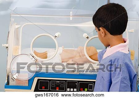 Stock Photograph - Close-up of a boy touching a baby boy in an incubator. Fotosearch