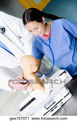 Stock Image - Girl examining a doll with a stethoscope and a male doctor standing beside her. Fotosearch