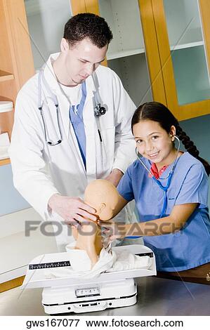 Stock Photo - Girl examining a doll with a stethoscope and a male doctor standing beside her. Fotosearch