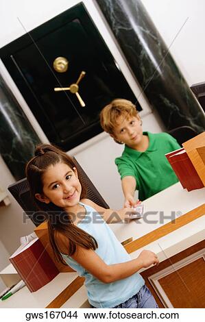 Portrait of a boy imitating a cashier at a bank giving money to a girl View Large Photo Image Picture - Portrait of a boy imitating a cashier at a bank giving money to a girl. Fotosearch