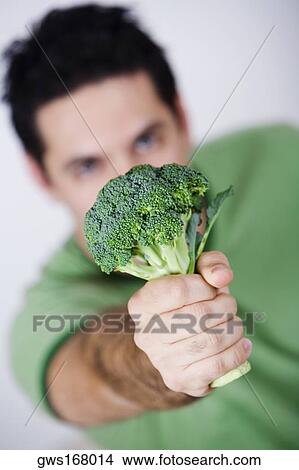 Picture - Close-up of a mid adult man holding a broccoli. Fotosearch