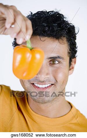 Close-up of a young man holding an orange bell pepper and smiling View Large Photo Image Stock Image - Close-up of a young man holding an orange bell pepper and smiling. Fotosearch