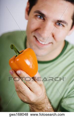 Stock Photo - Portrait of a mid adult man holding an orange bell pepper and smiling. Fotosearch