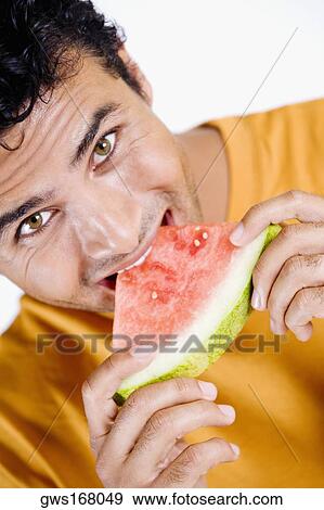 Portrait of a young man eating a slice of a watermelon View Large Photo Image Stock Photo - Portrait of a young man eating a slice of a watermelon. Fotosearch