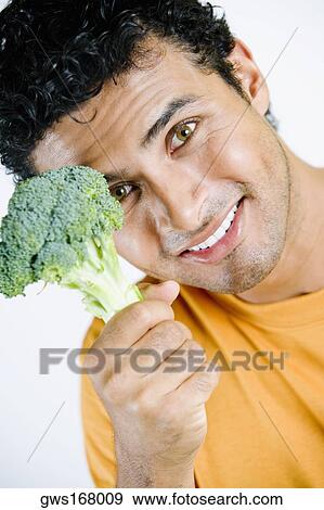 Stock Photo - Portrait of a young man holding a broccoli and smiling. Fotosearch