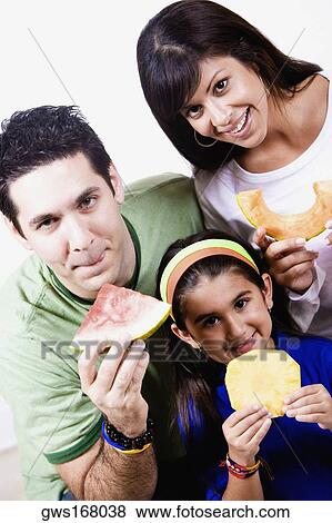 Portrait of a young woman and a mid adult man with their daughter holding slices of fruits View Large Photo Image Stock Photo - Portrait of a young woman and a mid adult man with their daughter holding slices of fruits. Fotosearch