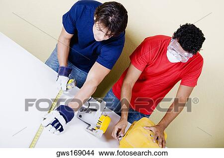 Mid adult man measuring with a measuring tape and a young man opening a toolbox View Large Photo Image Picture - Mid adult man measuring with a measuring tape and a young man opening a toolbox. Fotosearch