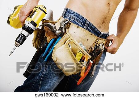 Stock Image - Mid section view of a man holding a drill machine. Fotosearch
