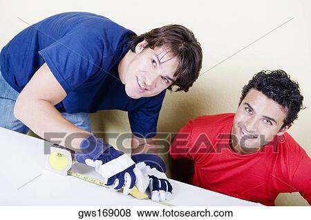 Portrait of a mid adult man measuring a board with a measuring tape and a young man sitting beside him View Large Photo Image Stock Photo - Portrait of a mid adult man measuring a board with a measuring tape and a young man sitting beside him. Fotosearch