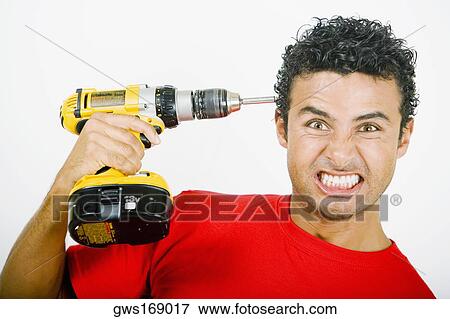 Portrait of a young man holding a drill machine against his head View Large Photo Image Stock Photo - Portrait of a young man holding a drill machine against his head. Fotosearch