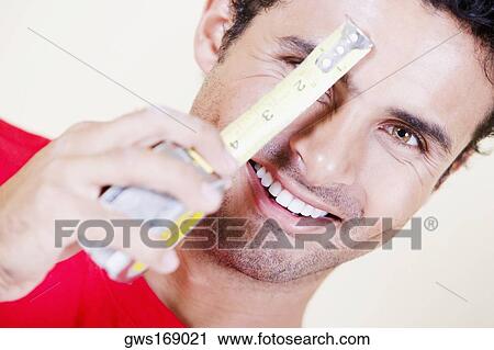 Portrait of a young man holding a measuring tape in front of his face and smiling View Large Photo Image Stock Image - Portrait of a young man holding a measuring tape in front of his face and smiling. Fotosearch