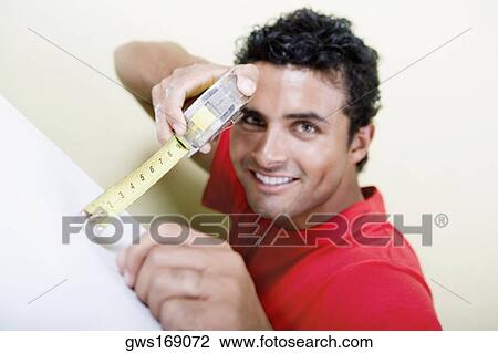 Stock Image - Portrait of a young man measuring with a measuring tape. Fotosearch